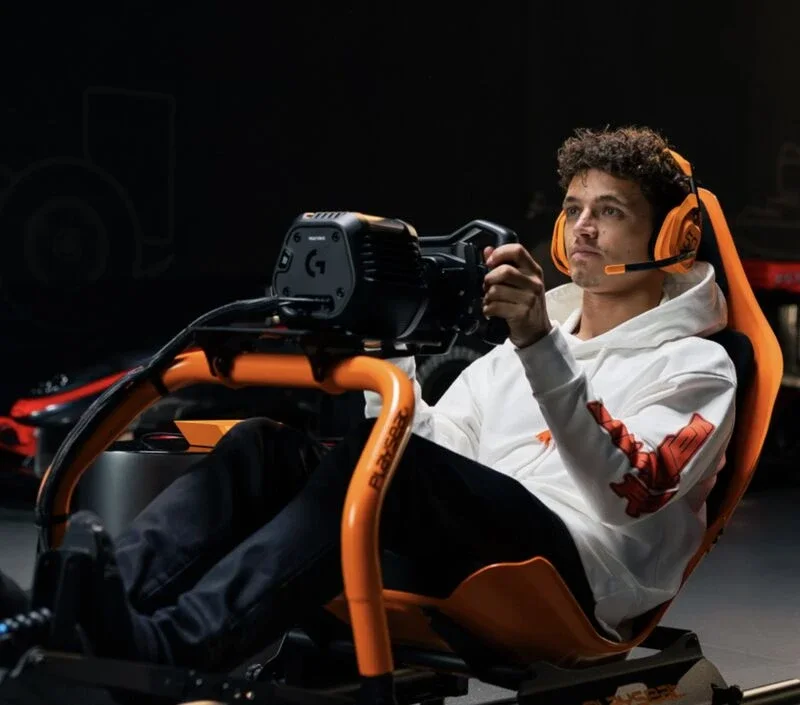 Reference look: a driver in an orange Playseat cockpit with a Logitech G RS50 wheel base and an orange ASTRO A50 headset